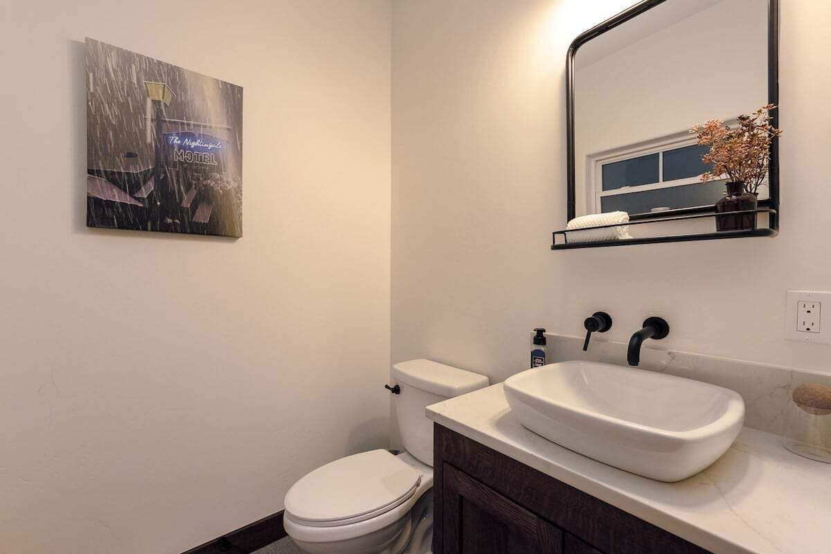 A bathroom with a white toilet, a white sink, a mirror, and a framed picture on the wall.