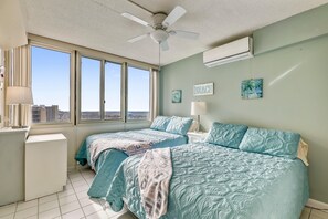 Un dormitorio con dos camas, un ventilador de techo, una ventana con vista a la ciudad y decoración en las paredes.