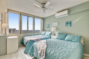 Ein Schlafzimmer mit zwei Betten, einem Deckenventilator, einer Klimaanlage, einem Fenster mit Blick auf die Stadt und Kunstwerken an den Wänden.