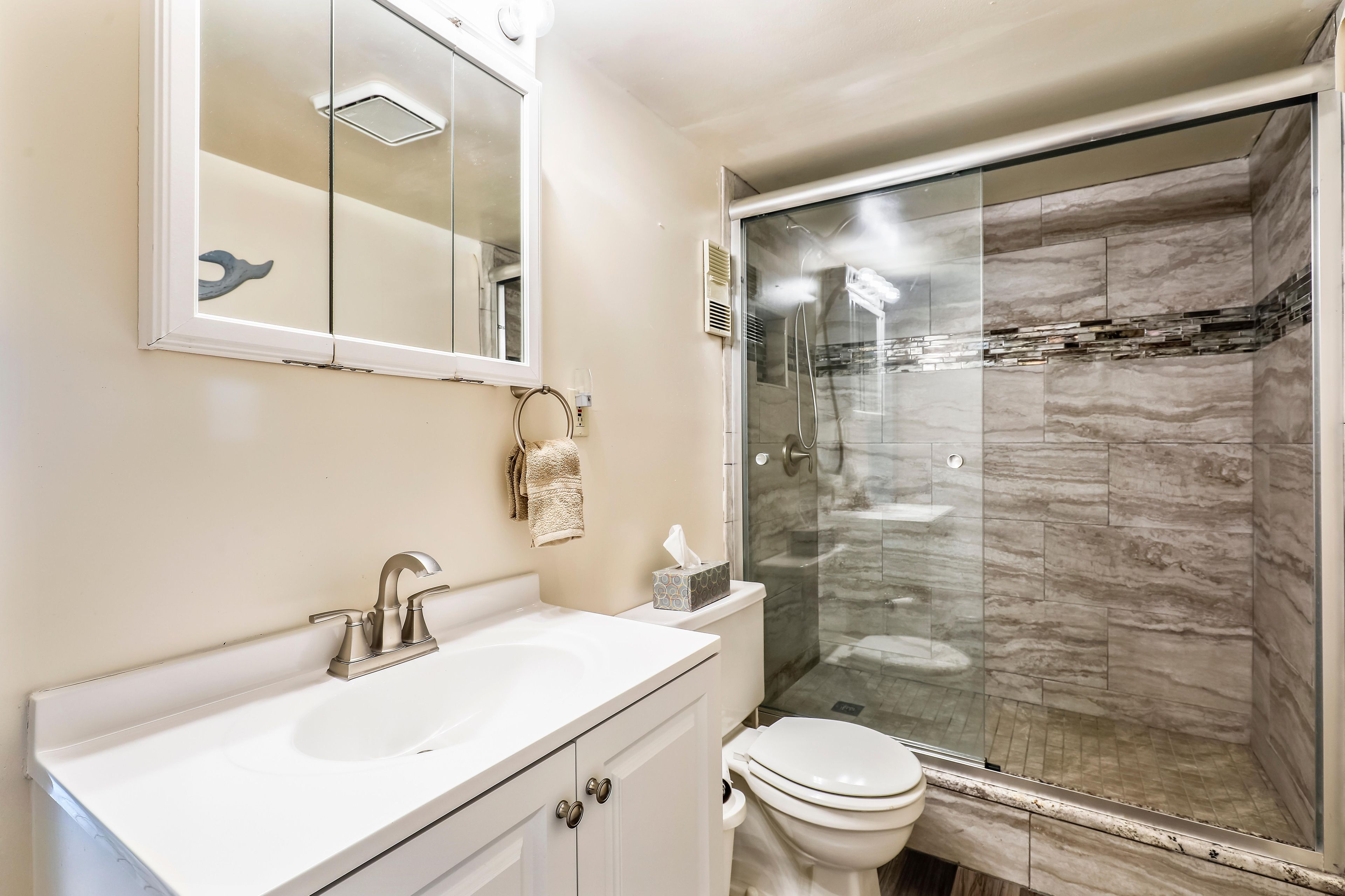 A bathroom with a white sink, a mirror, a towel rack, a toilet, and a glass-enclosed shower.