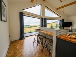 Una cocina con suelo de madera en patrón de espiga, una zona de bar con taburetes, un ventanal con vistas a un campo y una botella de champán en la encimera.