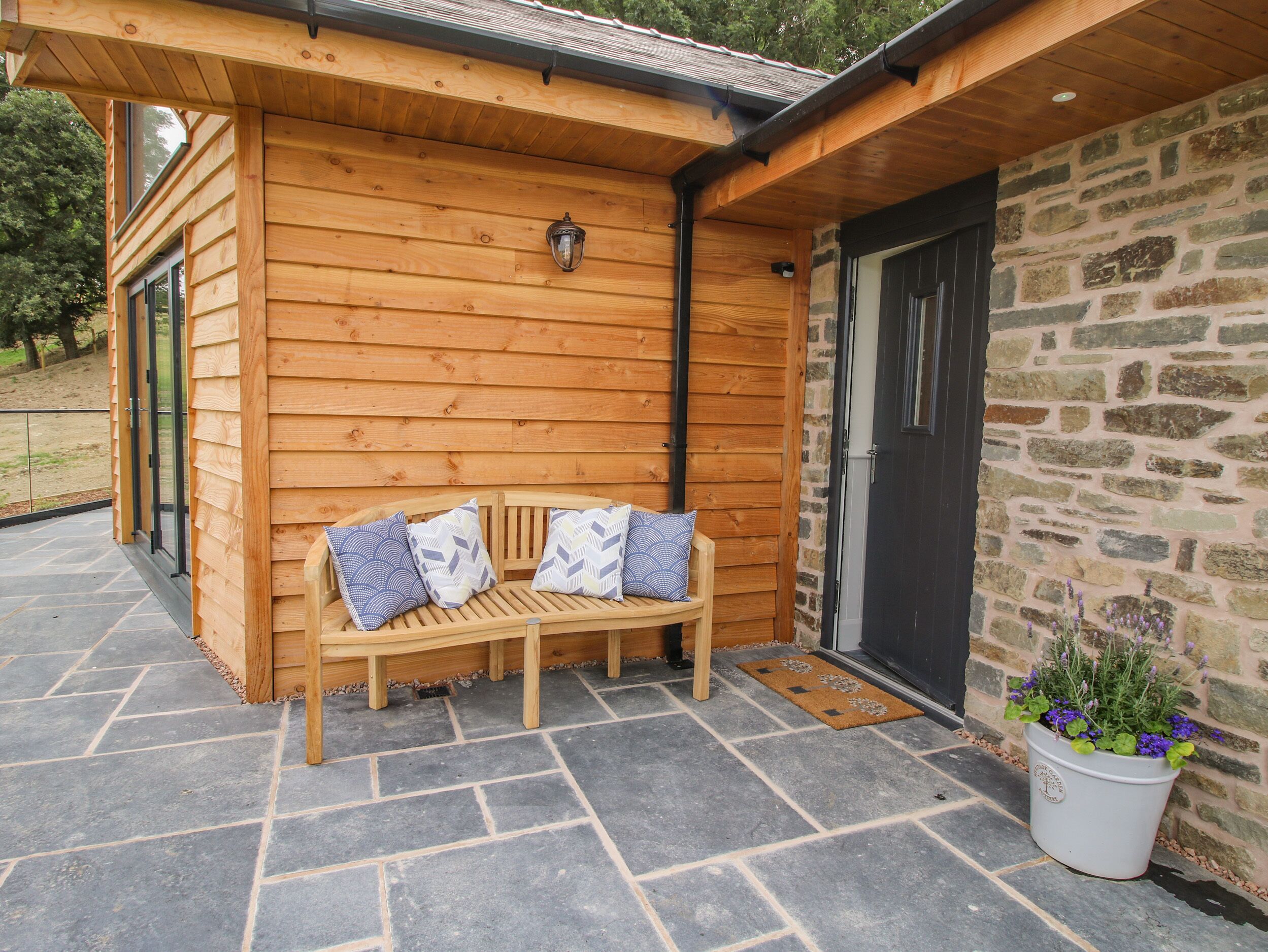 A wooden bench with cushions outside a building with a stone wall and a door.