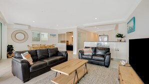 Un salon moderne avec un canapé en cuir noir, une table basse en bois et un coin repas comprenant une table et des chaises en bois.