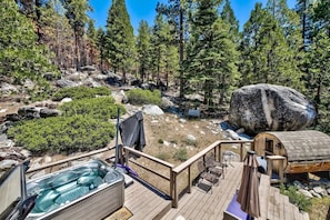 A hot tub on a wooden deck with a view of a forest and a large rock. - Reindeer A Frame Cabin, hot tub, pet friendly (South Lake Tahoe)
