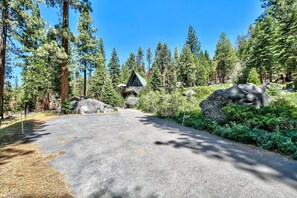 A forested area with a paved path leading to a cabin with a triangular roof. - Reindeer A Frame Cabin, hot tub, pet friendly (South Lake Tahoe)