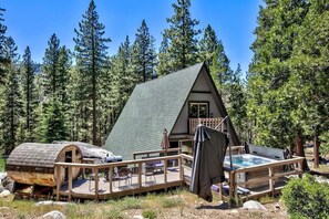 Eine Hütte mit einer Terrasse, einem Whirlpool und einer überdachten Sitzgruppe im Freien, umgeben von Bäumen.