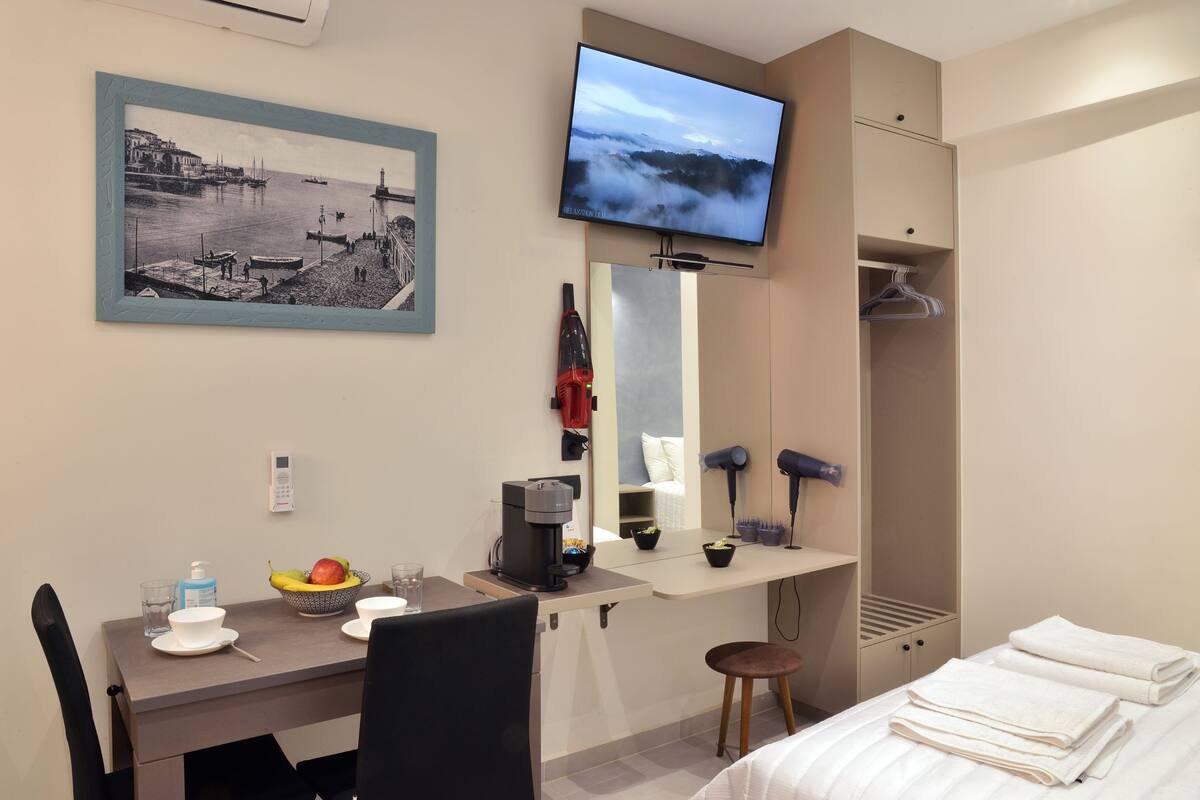 Habitación de hotel con cama, escritorio con cafetera, televisión, espejo y un cuadro en la pared.