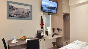 Habitación de hotel con cama, escritorio con cafetera, televisión, espejo y un cuadro en la pared.