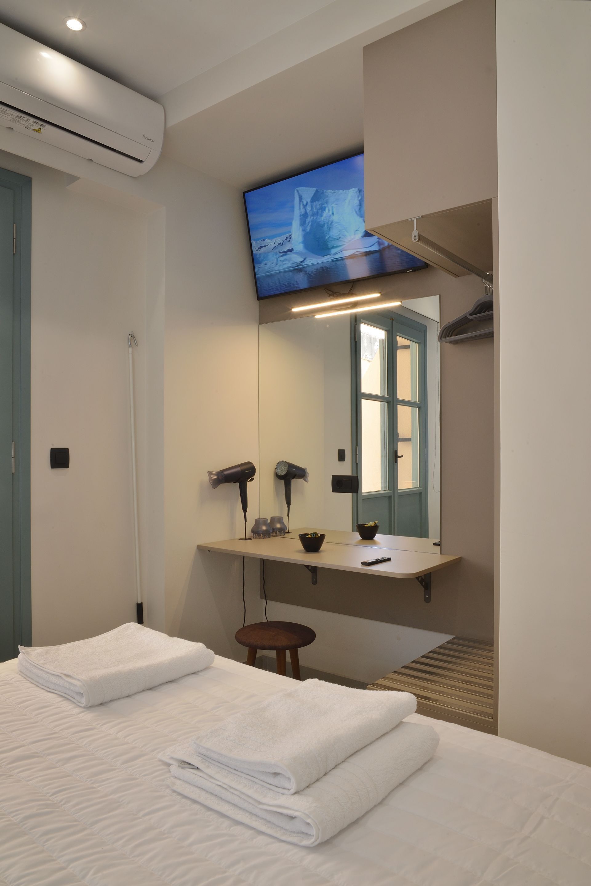A hotel room with a bed, a vanity with a mirror, a mounted TV, and a hairdryer.