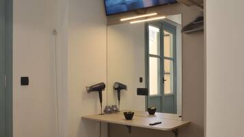 A hotel room with a bed, a vanity with a mirror, a mounted TV, and a hairdryer.