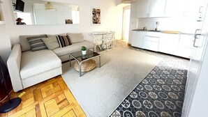 A modern living room with a sofa, coffee table, and a dining area with chairs. There is a kitchen area with cabinets and a sink. - Acogedor piso cerca al Parque El Retiro FREE WIFI (Madrid)