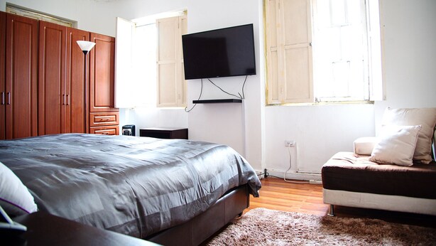 Quarto com cama, TV na parede, armários de madeira e janela.