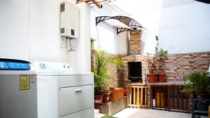 Uma área de lavanderia com máquina de lavar, parede de tijolos e plantas em vasos.