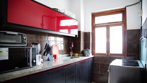 Uma cozinha com armário superior vermelho, micro-ondas, liquidificador e panela de arroz sobre a bancada.