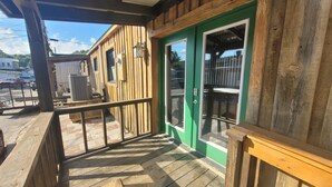 A wooden deck with a green door and windows, a railing, and a view of parked cars and buildings in the background. - Downtown Bryson City 2 Bedroom Apartment, Perfect for Polar Express! (Bryson City)