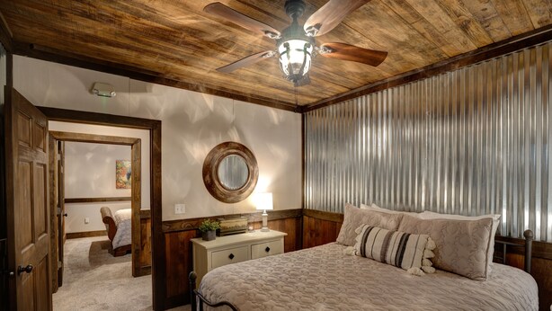A bedroom with a wooden ceiling, a bed with a quilt, a nightstand with a lamp, and a window with blinds. - Downtown Bryson City 2 Bedroom Apartment, Perfect for Polar Express! (Bryson City)