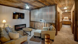 A living room with a fireplace, leather sofas, a TV, and a kitchen in the background. - Downtown Bryson City 2 Bedroom Apartment, Perfect for Polar Express! (Bryson City)