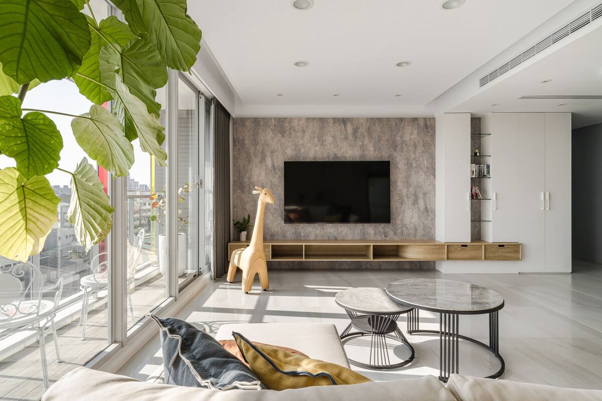 A modern living room with a large TV, a giraffe statue, and a balcony with city views.