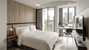 A modern hotel room with a large bed, a desk with a computer, a TV, and a view of the city. - 1LI7E HOTEL (Taichung)