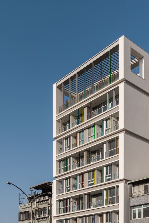Un edificio de varios pisos con un diseño arquitectónico moderno, con balcones de barandillas de vidrio y un cielo despejado al fondo.