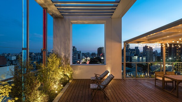 A rooftop terrace with a wooden deck, two cushioned chairs, a table, and a view of the cityscape at dusk. - 1LI7E HOTEL (Taichung)