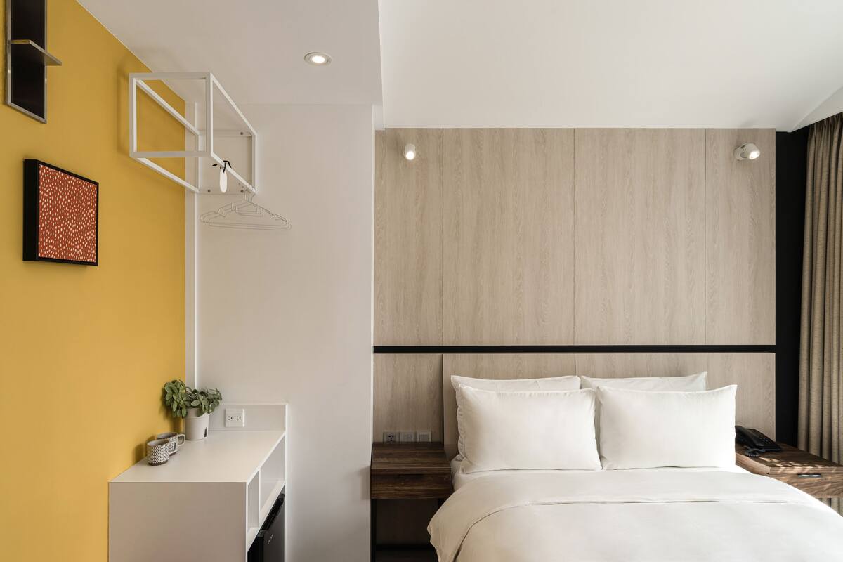 A modern hotel room with a bed, bedside table, and a small desk with a plant and a mug.