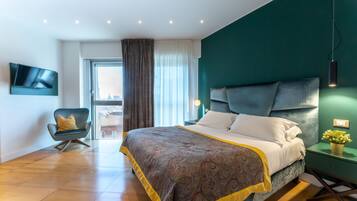 Ein modernes Hotelzimmer mit einem großen Bett, einem an der Wand befestigten Fernseher, einem Sessel und Blick auf die Stadt durch das Fenster.