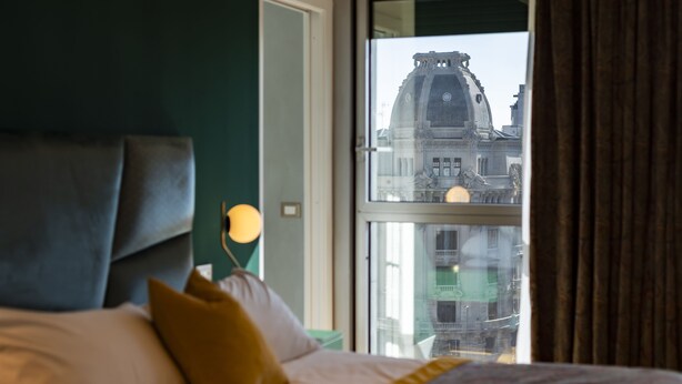 A bed with a headboard, pillows, and a view of a building through a window. - Missori Suites (Milan)