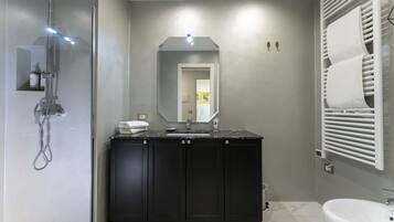 Une salle de bain moderne avec une douche à parois de verre, des meubles de couleur sombre, un lavabo blanc et un grand miroir.