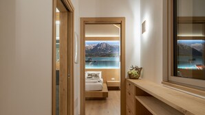 A hallway with a wooden floor leading to a bedroom with a view of a lake and mountains.