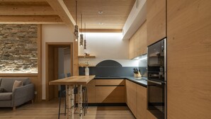 A modern kitchen with wooden cabinets, a built-in oven, and a stone wall backsplash. - Casera Cal De Mez Sot - Wellness Chalet (Chies d´Alpago)