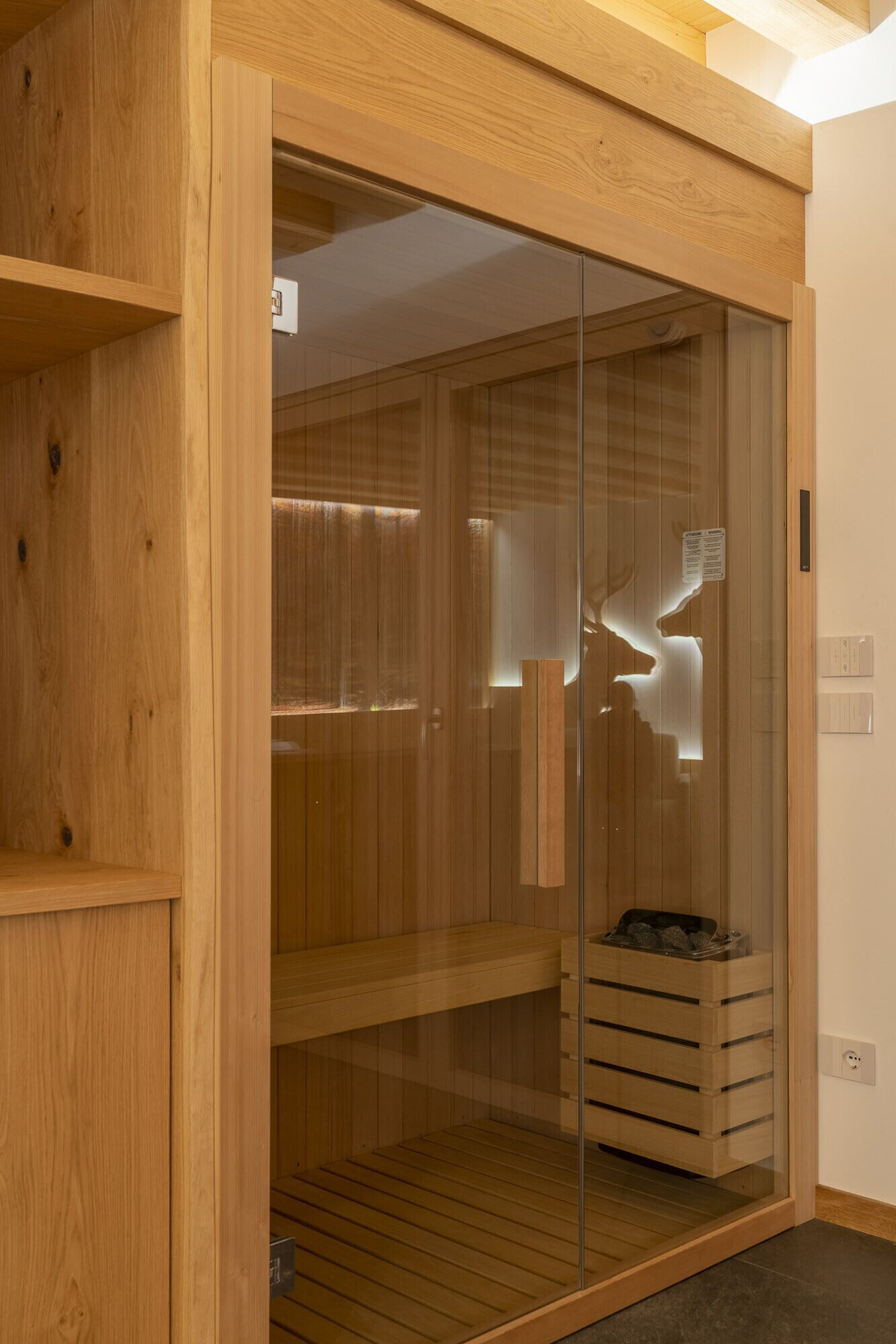 Una sauna de madera con puerta de vidrio, un banco de madera y un pequeño estante de madera.