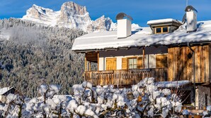 A wooden cabin with a snow-covered roof, a wooden deck, and a mountain backdrop. - CHALET INES - Studio Apartment 3 (Vodo Cadore)