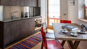A modern kitchen with dark cabinets, a wooden countertop, and a red chair. - CHALET INES - Studio Apartment 3 (Vodo Cadore)