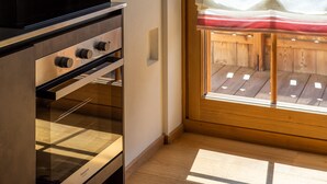 An interior with a modern kitchen featuring stainless steel appliances, a wooden floor, and a view through a window with a wooden deck outside. - CHALET INES - Studio Apartment 3 (Vodo Cadore)