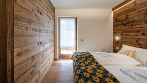 Un dormitorio con paredes de paneles de madera, una cama con ropa blanca y vistas a través de una puerta abierta.