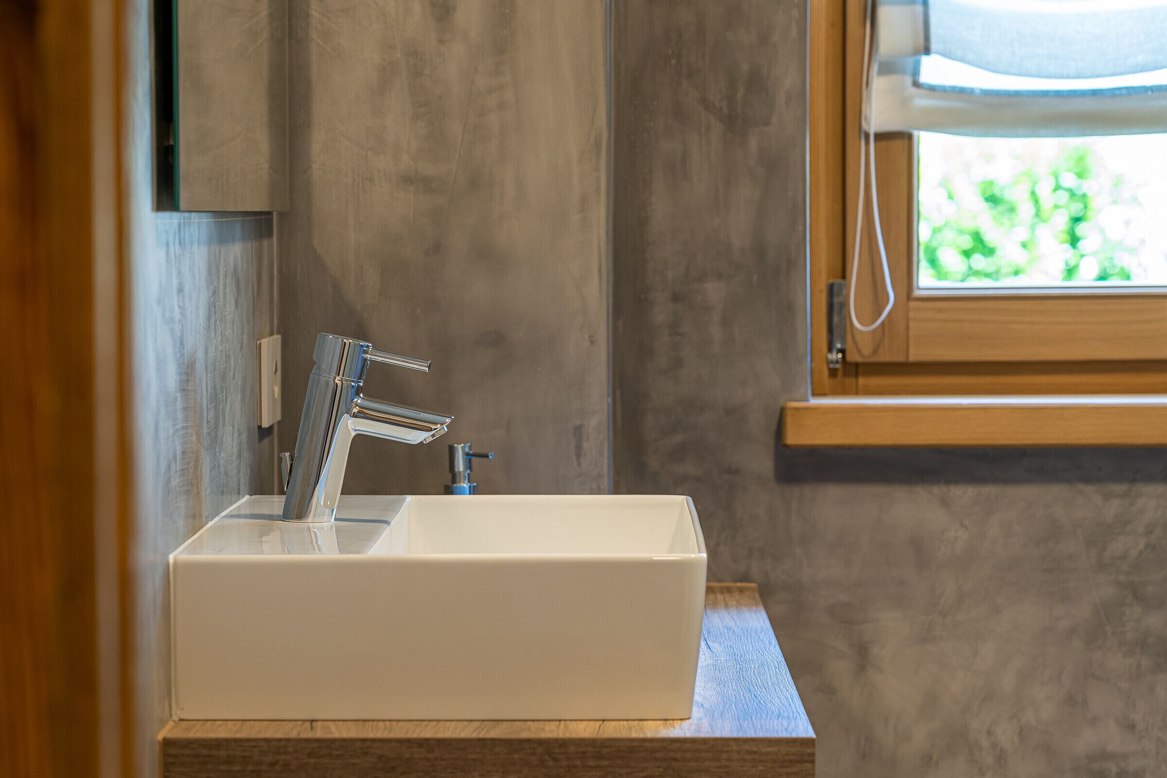 A bathroom with a white rectangular sink, a modern faucet, and a wooden countertop.
