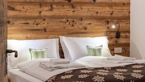 A wooden-paneled bedroom with a bed, pillows, and a nightstand. - CHALET INES - Appartamento 1 (Vodo Cadore)