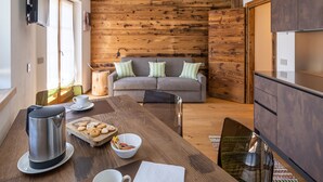 A cozy dining area with a wooden table, a sofa, and a kitchen area in the background. - CHALET INES - Appartamento 1 (Vodo Cadore)