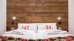 Un lit bien fait, avec du linge de lit blanc et une couverture à motifs floraux, deux lampes de chevet et une tête de lit en bois.