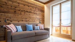 Un salon moderne avec un mur en bois, un canapé beige agrémenté de coussins à rayures et une grande porte-fenêtre coulissante donnant sur un espace extérieur.