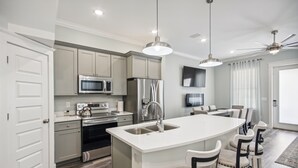 Una cocina moderna con una isla central, electrodomésticos de acero inoxidable, iluminación colgante y un comedor con sillas.