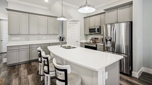 Una cocina moderna con armarios grises, electrodomésticos de acero inoxidable y una isla central con taburetes.