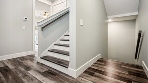 Una escalera moderna con escalones de madera y paredes blancas, que conduce a un rellano con ventilador de techo.