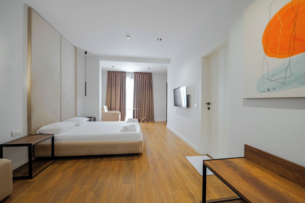 Una habitación de hotel moderna con una cama grande, un escritorio, una silla, un televisor y un cuadro en la pared.