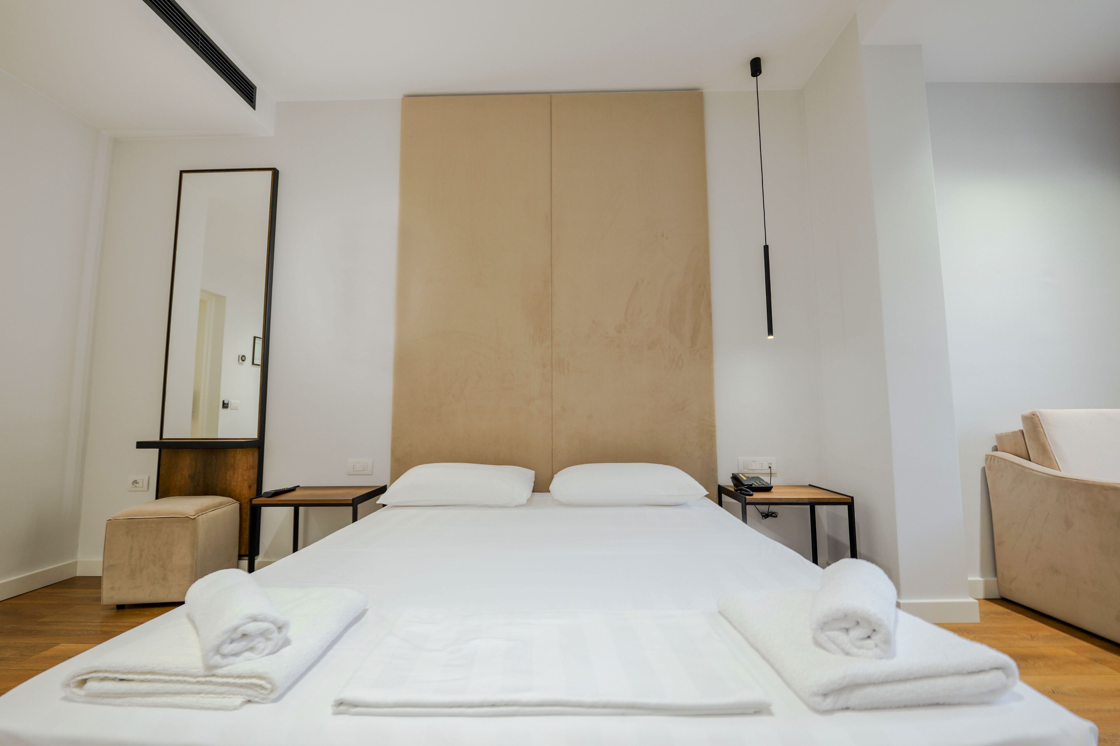 A modern hotel room with a large bed, a bedside table, a nightstand, a chair, and a large mirror.