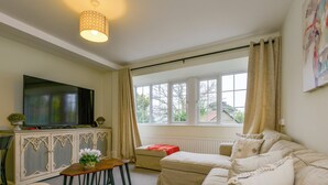 A living room with a television, sofa, and a window with curtains. - Valley View (Teignmouth)