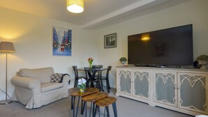 A living room with a sofa, a dining table with chairs, a TV on a cabinet, and a lamp. - Valley View (Teignmouth)