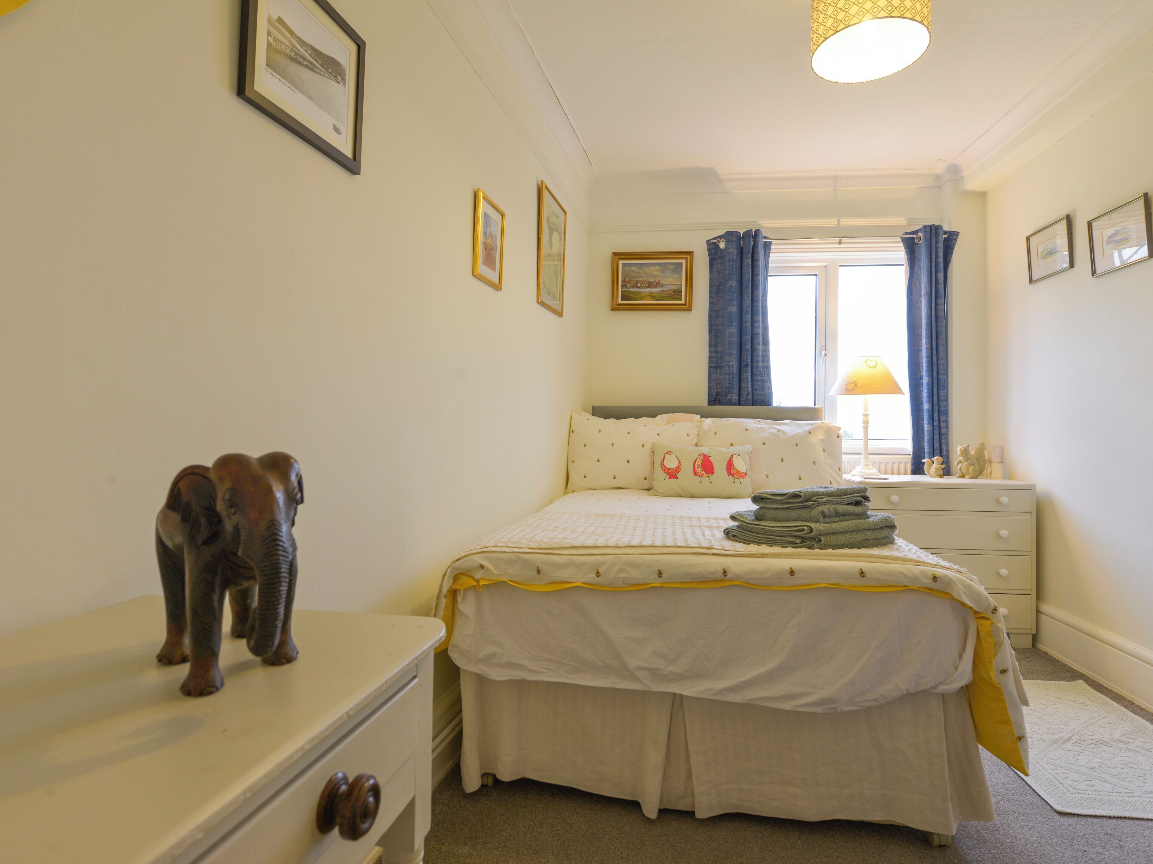 A bedroom with a bed, a dresser, a nightstand, and a window with curtains.