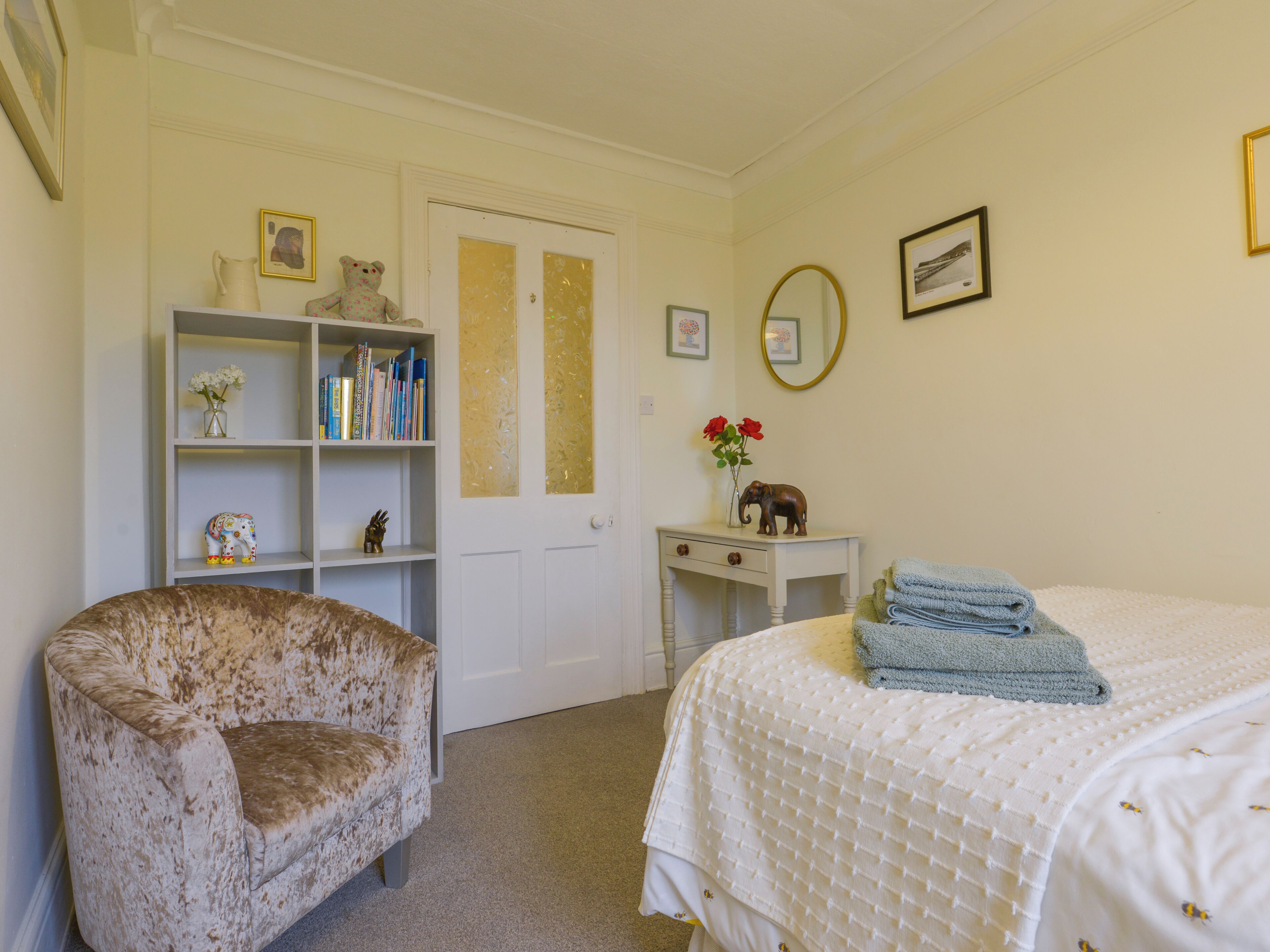 A bedroom with a bed, a chair, a bookshelf, a dresser, and a door.